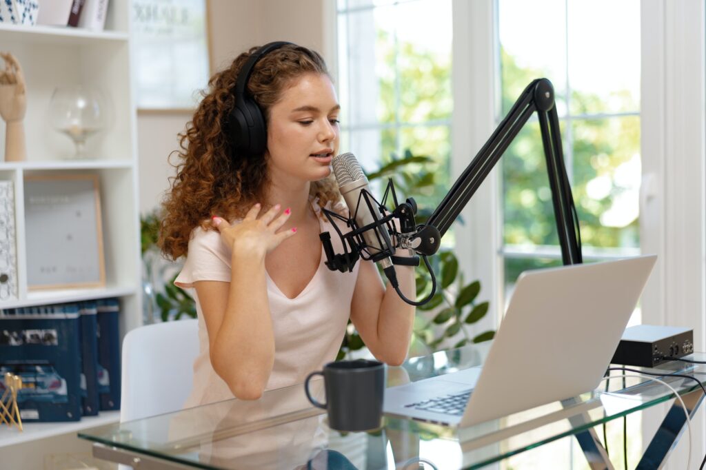 Young curly female recording podcast from home and talking into a microphone