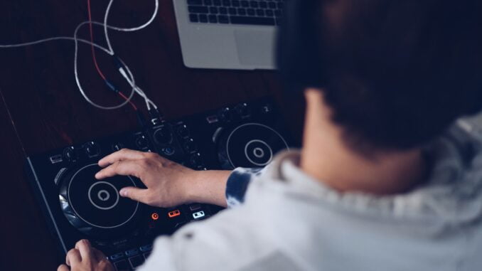 Young man using laptop computer and DJ soundboard, turntable, audio equipment